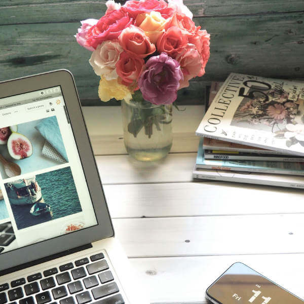 image of bouquet of roses in a glass jar next to a stack of magazine and a laptop computer