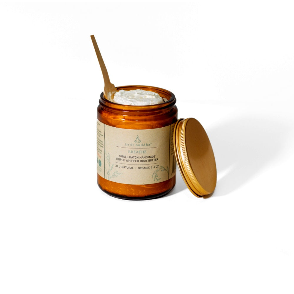 image of amber colored glass jar with a craft paper label.  Jar is open and filled with cream colored lotion with a wooden paddle in it.