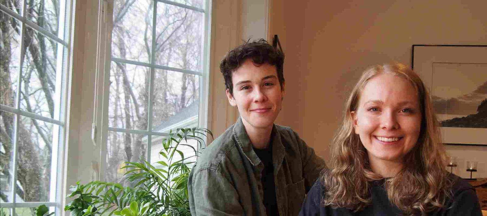 image of the two owners of Queer Candle Company, sitting in front of a window looking outdoors