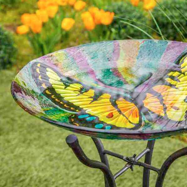 partial image of a glass birdbath with a colorful butterfly image on it, sitting on a black iron stand