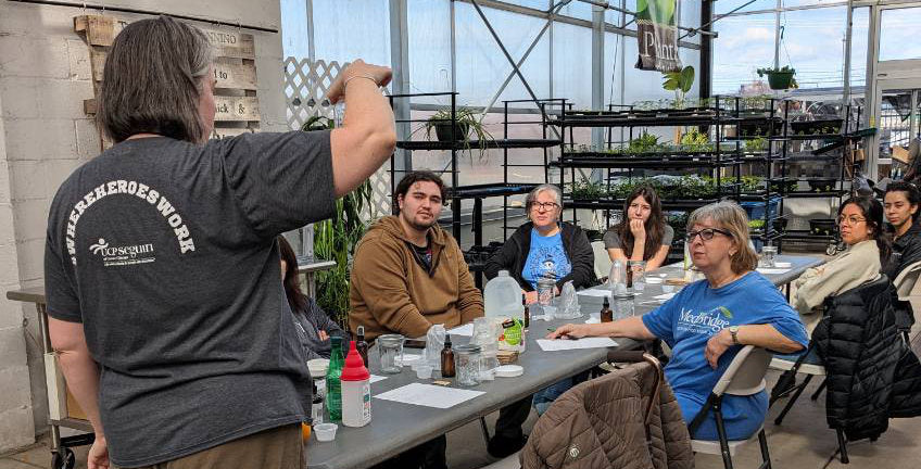 image of woman in grey shirt demonstrating to a group of people sitting at a table