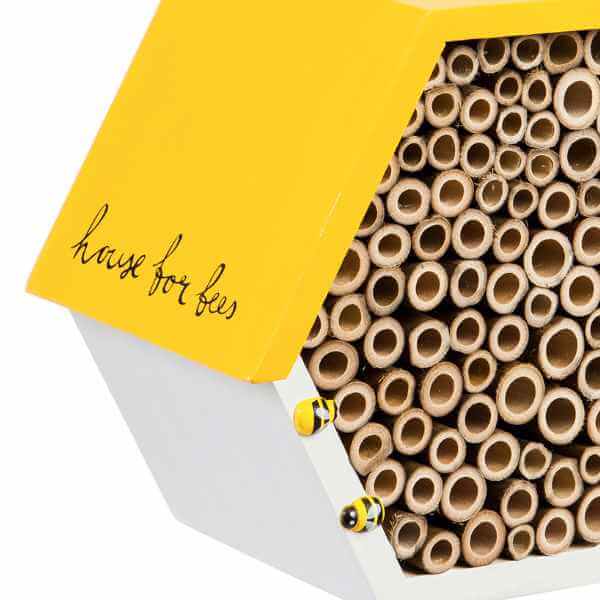 image of half of a hexagon shaped bee house with yellow top, white bottom, filled with tubes
