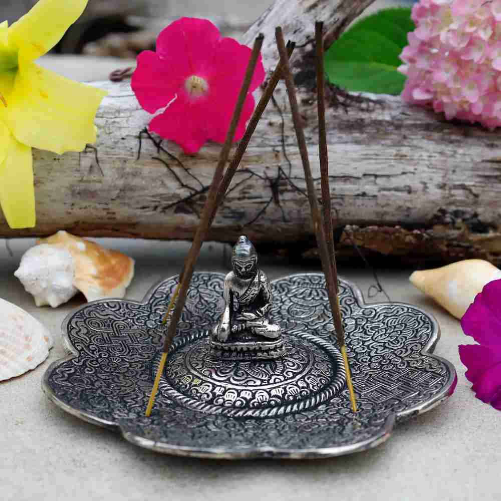 image of a silver with black accent incense holder in a scalloped edge shape with a buddha figure sitting on it.