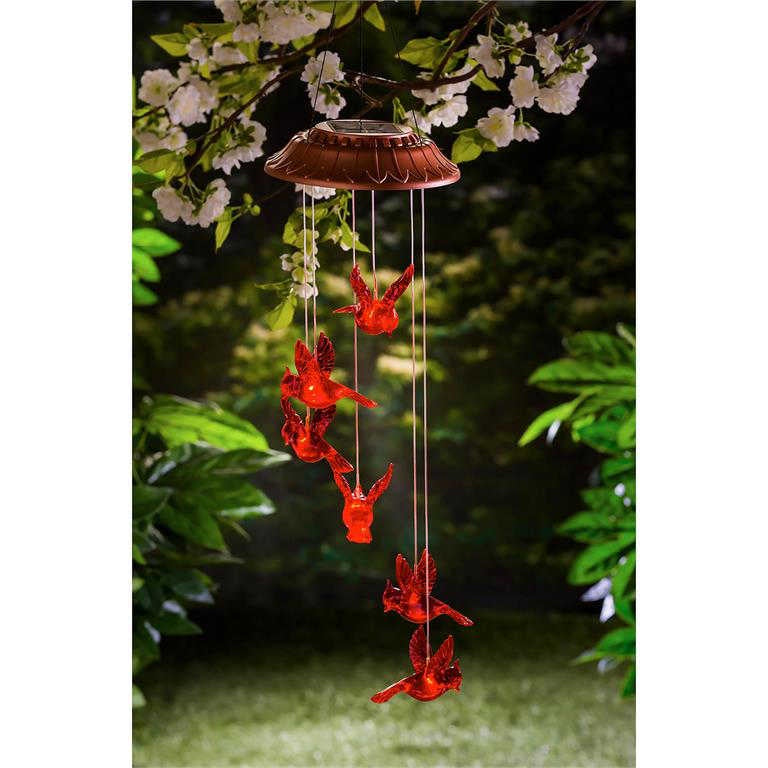 Decorative wind chime with red  cardinal shapes hanging from a brown base against a green foliage background.