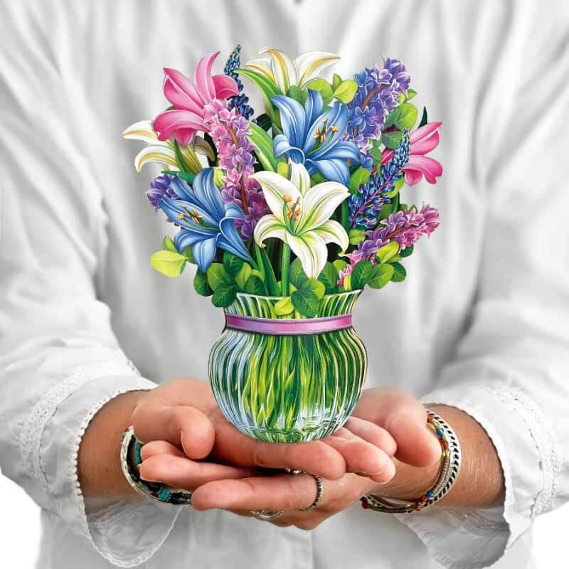 image of a person in white holding a paper bouquet of multi colored flowers in a glass vase looking base