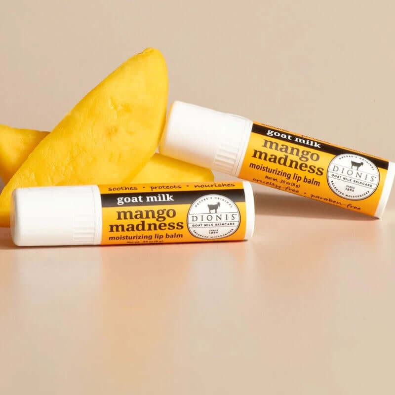 image of two tubes of lip balm in bright yellow laying in front of two wedges of fresh mango