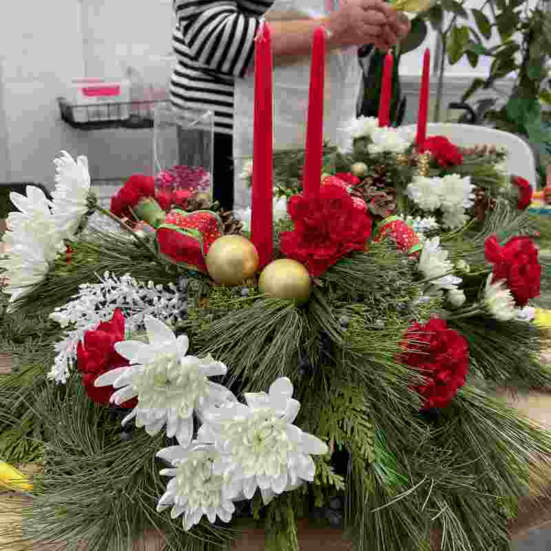 image of a tabletop centerpiece using various fresh evergreens with two red taper candles and a red and green plaid bow