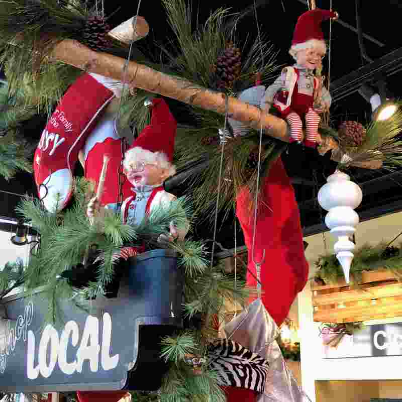 image of two elf dolls hanging from the ceiling on birch poles, with Christmas stocking and a local sign and large white finial ornament