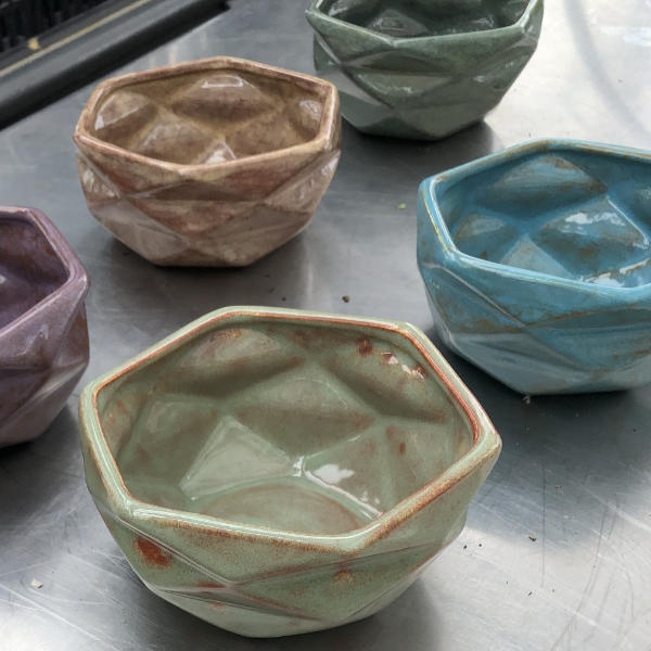 image of several hexagonal shaped ceramic pots with faceted sides in varying colors of green blue and peach
