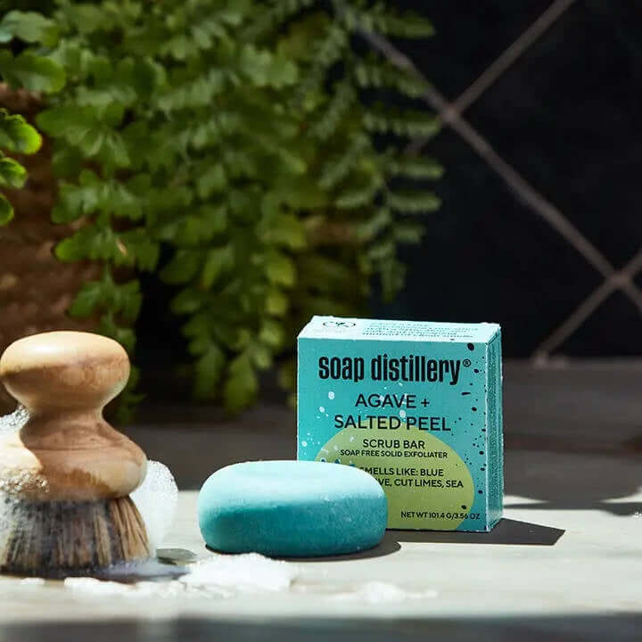 Blue scrub bar and packaging with 'Soap Distillery' branding on a surface with a plant in the background.