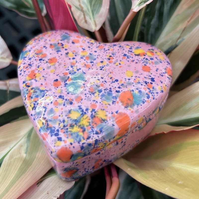 Colorful heart-shaped object with a multicolored speckled pattern on a plant background