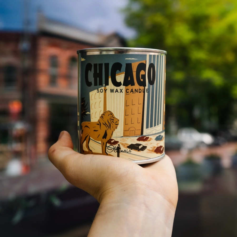 image of hand holding a round candle with a label showing drawings of chicago buildings and the lions from the Art Institute