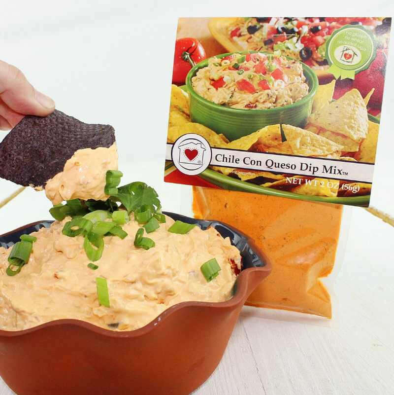 Chile Con Queso Dip Mix with a tortilla chip being dipped into it, next to a package of the dip mix.