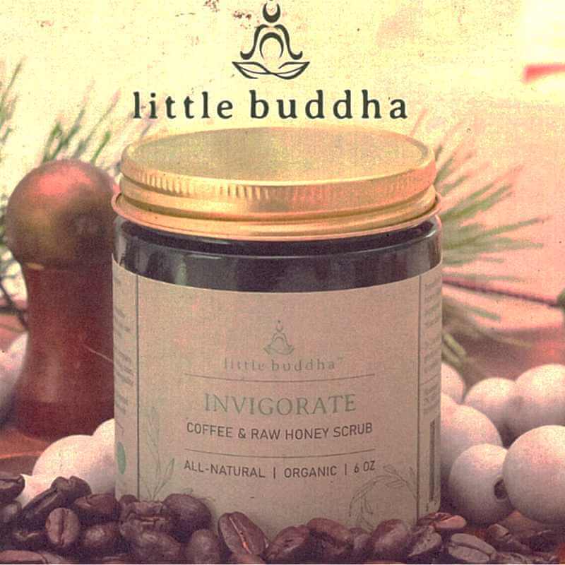image of dark brown jar with tan label and brass lid.  Little buddha logo above.  Sitting amongst coffee bean and a white beaded necklace