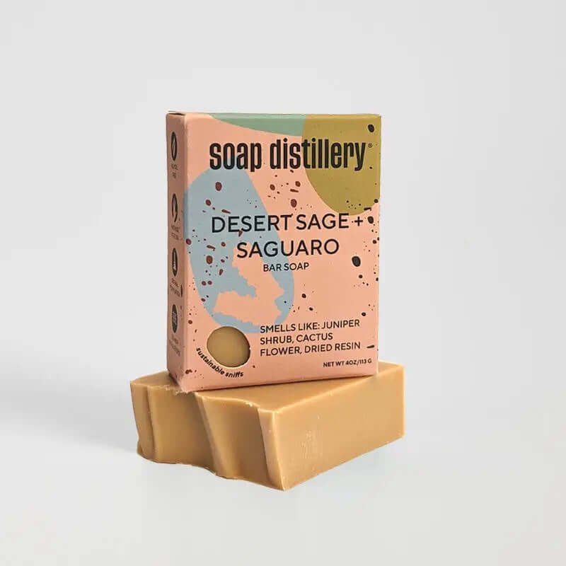 image of box of soap in peach, blue, light green and mustard colors sitting on a bar of soap in a golden color