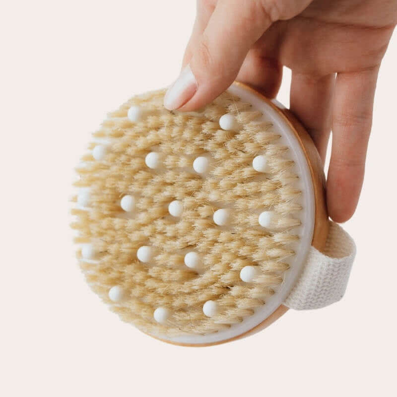Hand holding a round brush with bristles and a wooden handle on a light background