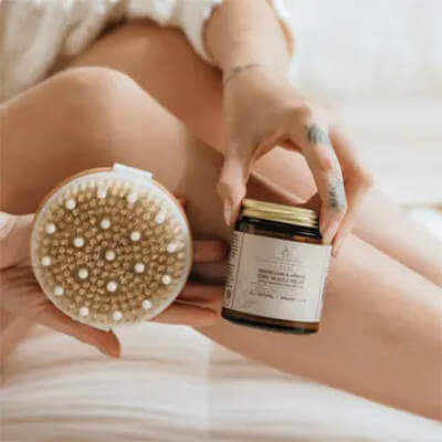 Person holding a skin care brush and jar of cream on a soft surface