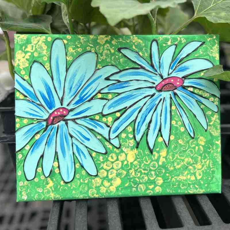 image of canvas with textured green background and two large daisy like flowers with blue petals
