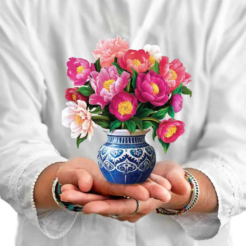 image of person in white holding a paper bouquet of multiple colored peonies in a blue and white vase
