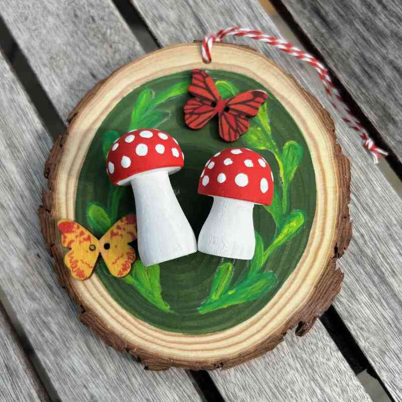 Decorative wooden ornament with red and white mushrooms and butterflies on a green background.