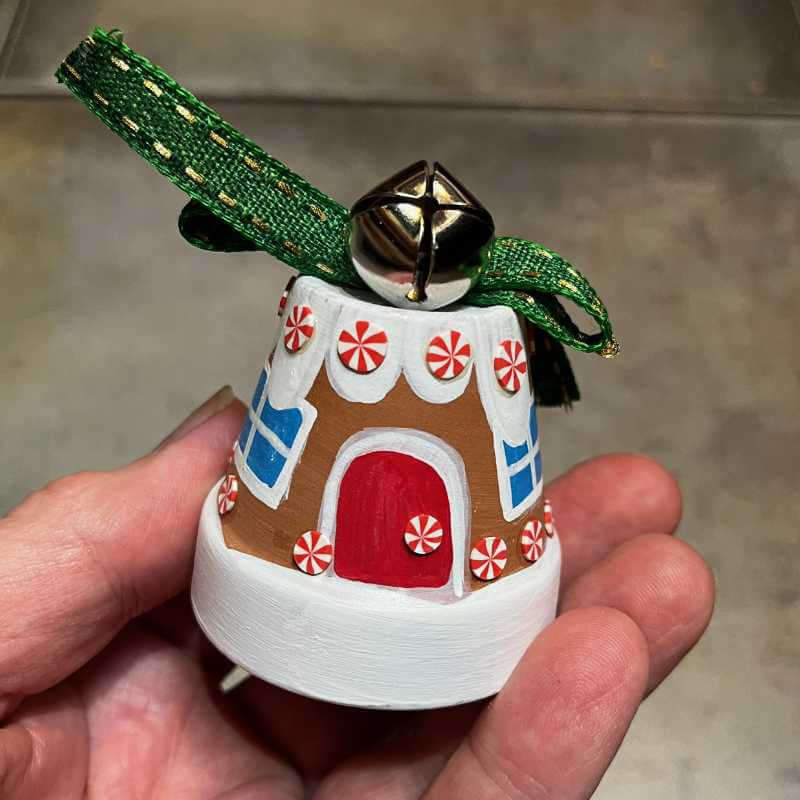 image of a hand holding a small ornament painted like a miniature gingerbread house