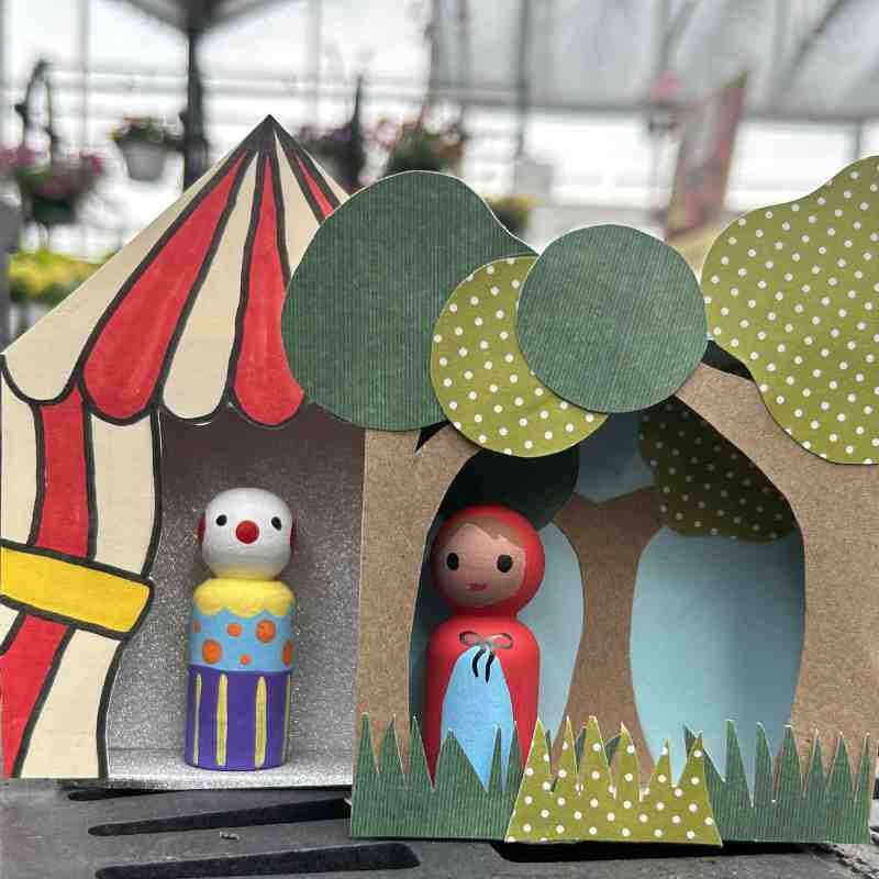 image of two small paper scenes each with a small person made of a small painted wooden peg