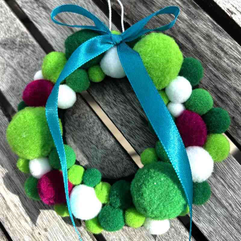 Colorful pom-pom wreath with a blue ribbon on a wooden surface