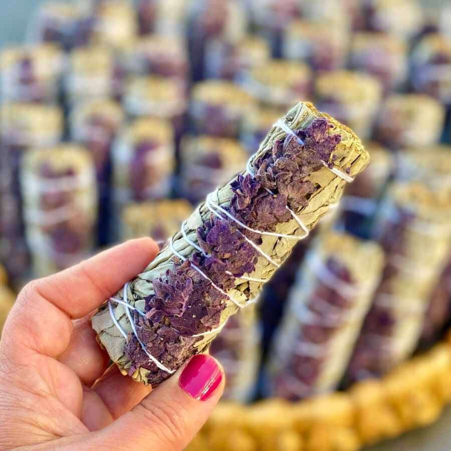 photo of a hand holding a bundle of dried white sage and lavender tied with white string