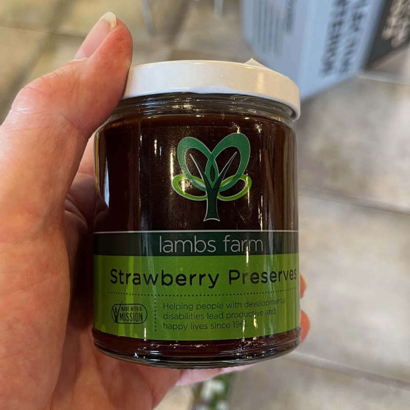 Hand holding a jar of Lambs Farm Strawberry Preserves with a green label.