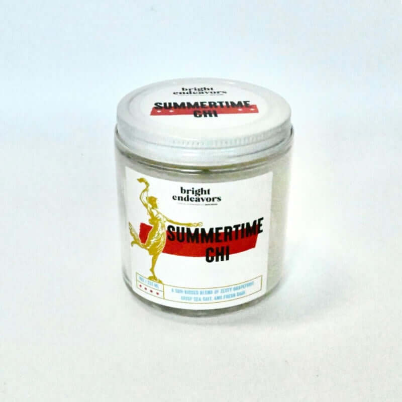 image of round glass jar candle with white lid.  Label is white with a drawing of a woman holding a torch and a red stripe with summertime chi written in front of stripe