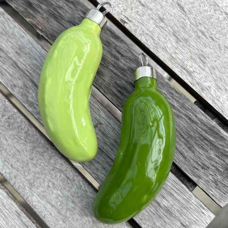 Two green pickle-shaped ornaments on a wooden surface