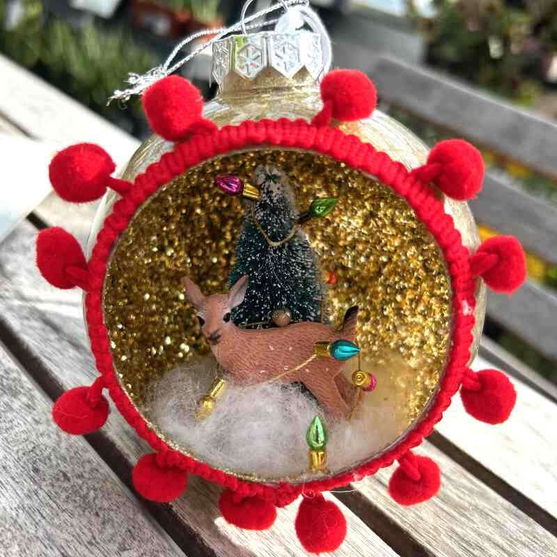 glass globe with small deer figurine inside and red pom poms surrounding the opening