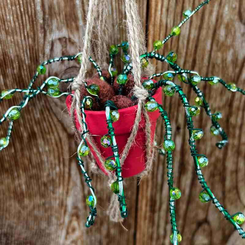 Decorative hanging plant with green beads and a red pot on a wooden background