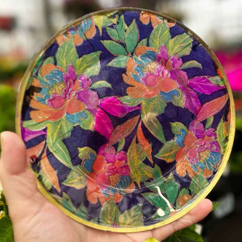hand holding a small round plate with a floral design in multiple bright colors