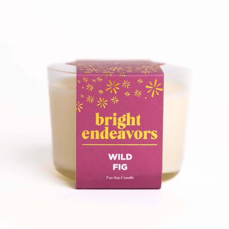 image of off white candle in clear glass jar with deep pink/purple paper wrap label