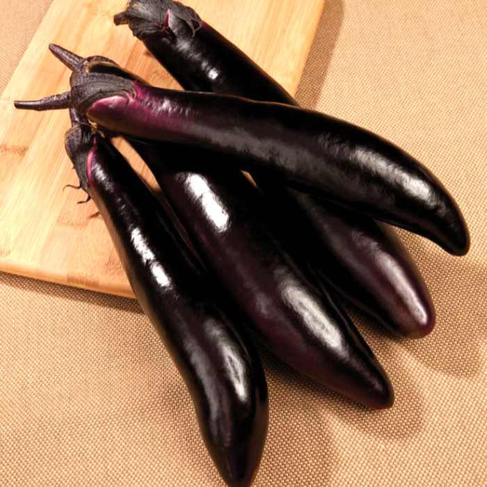 image of four long dark purple eggplants grouped on a surface, partially on a wooden cutting board