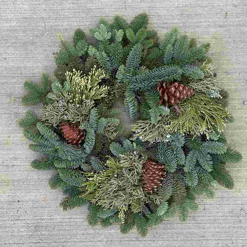 fresh wreath made of several different kinds of evergreens, with three pine cones