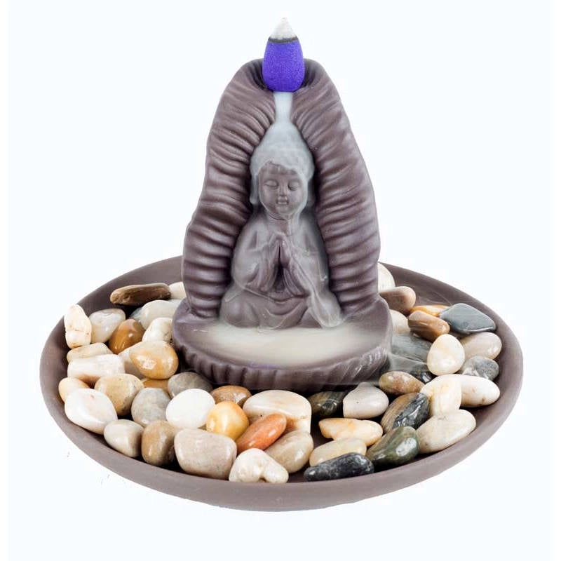 image of incense burner featuring a small image of a buddha praying and sitting on a circular base filled with small pebbles.  An incense cone at the top is sending smoke down around the buddha figure
