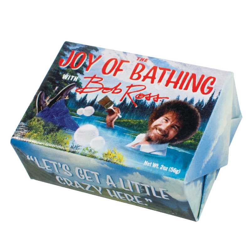 image of rectangular bar of soap in paper wrapper with a painting of a landscape with lake and trees, and a photo of Bob Ross holding a paintbrush.  Joy of Bathing with Bob Ross written on front of package