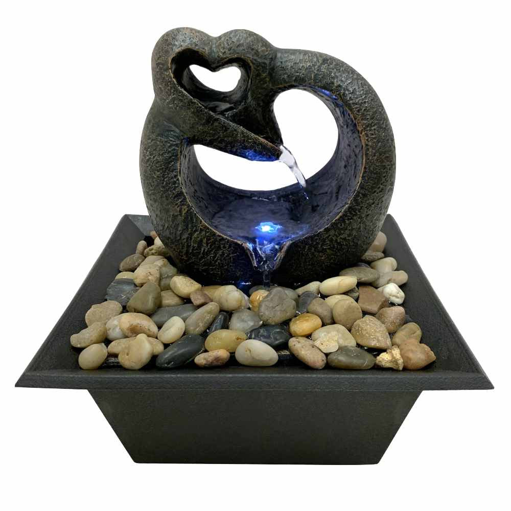 image of a small tabletop fountain with a square base covered in small stones, and a heart shaped upper portion with water coming out.