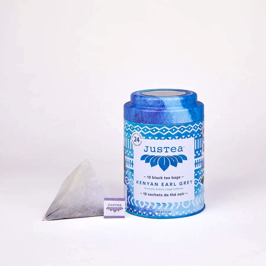 image of round tea tin in bright blue with blue and white logo and geometric designs.  Triangular tea bag to left of tin