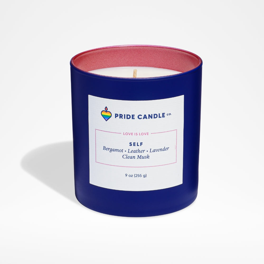 image of white candle in round glass jar in a bright deep blue exterior with frosted pink interior.  Square white label on the front with Pride Candle logo and candle info on it.