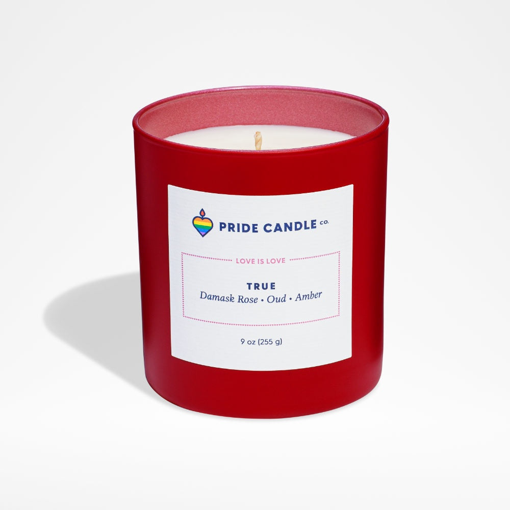 image of white candle in red round glass jar, with frosted red interior.  Square white label with Pride logo and candle info