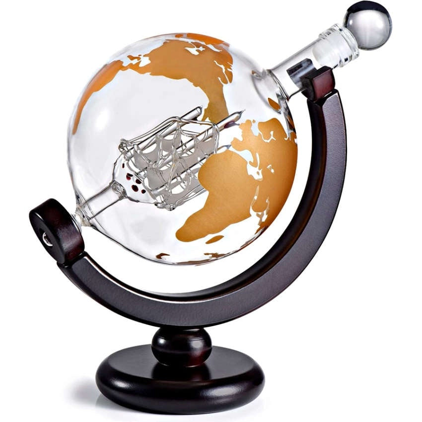 image of a globe shaped glass decanter with the world map etched in gold, with a blown glass miniature ship inside.  Sitting on an angle on a dark wood base