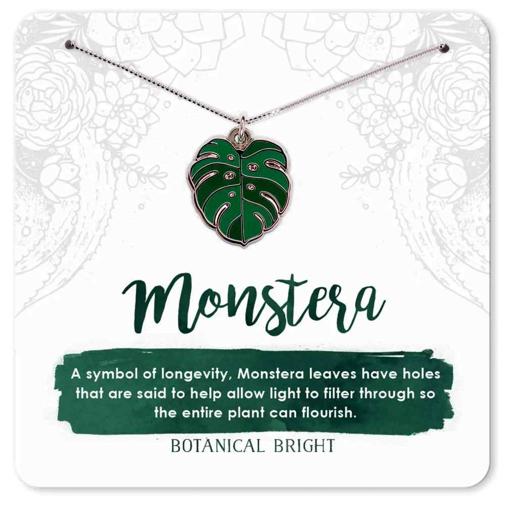 image of necklace with a monstera leaf shape in shades of medium and dark green.  On a card with description in green and white
