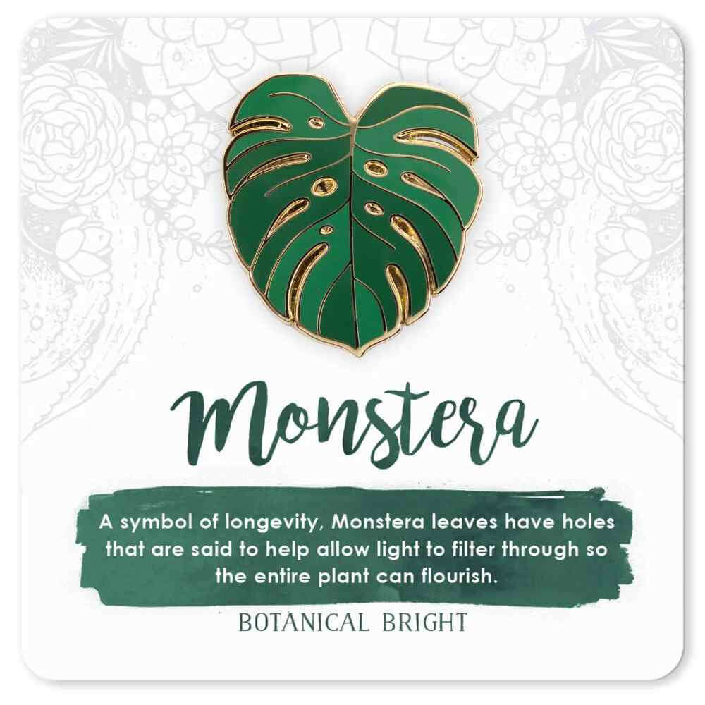 image of pin in the shape of a monstera leave in shades of medium and dark green.  On a card with description in green and white.