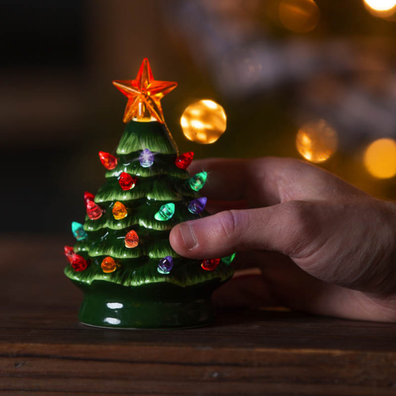 image of a human hand holding one of the small ceramic trees with the LED lights turned on