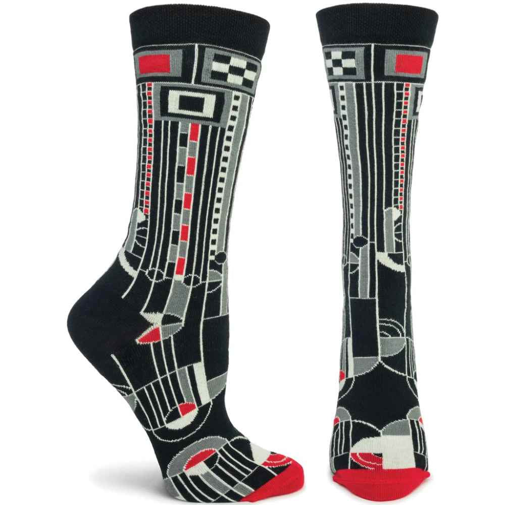image of two socks in feet.  One on left is seen from the side, the one on the right is seen from the front.  Design has a black background, with a rectangular geometric design in white, grey and red