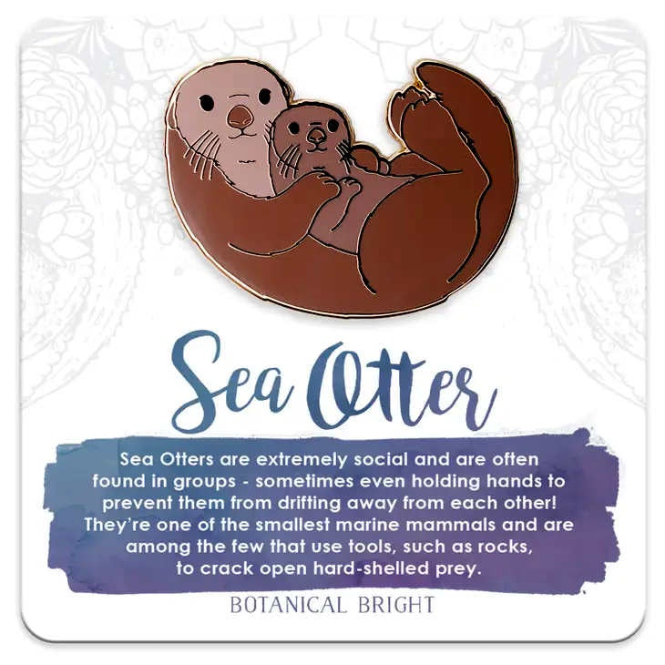 image of pin in the shape of a sea otter holding a baby otter.  In shades of light to medium brown.  On a card with description in blueish purple and white