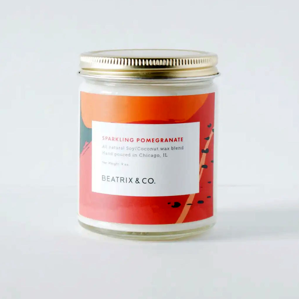 image of round jar candle with bright red and orange abstract design,  White rectangle on front with description of candle